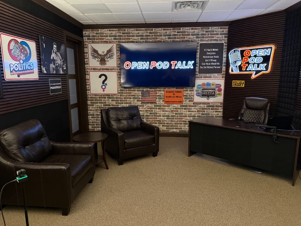 Open Pod Talk podcast studio interior with brick wall, desk, neon sign, and wall decor