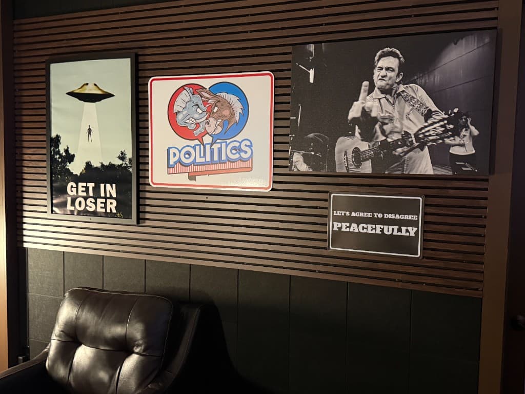 Studio wall art including politics heart sign, UFO poster, Johnny Cash print, and agree to disagree peacefully sign